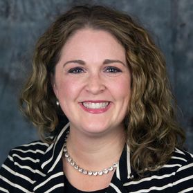 Headshot of WVU administrator Kristen Shipp. She is pictured in front of a marbled blue and gray background wearing a black and white striped jacket. She has shoulder length, wavy, light-colored hair. 