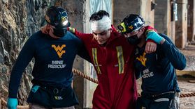 Two members of the WVU Mine Rescue Team help a person with a white bandage around their head.