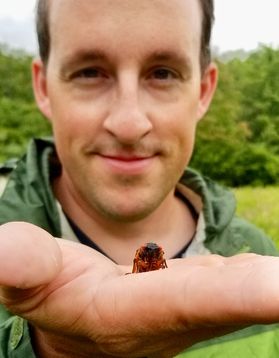a man holds a bug in the palm of his hand in front of his face