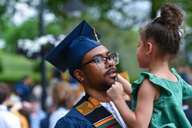 Black man in cap and gown smiles at a young girl