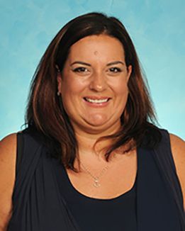 Headshot of WVU Medicine professor Megan Burkart. She is pictured against a light blue background and is wearing a dark colored sleeveless top. She has long brown hair. 