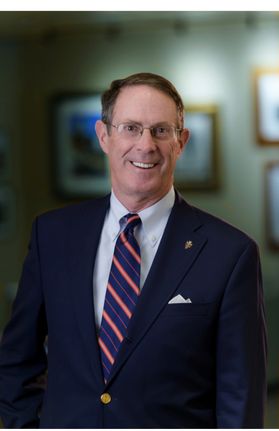 Headshot of oil executive Benjamin Ashby Hardesty. He is pictured inside with a wall of framed items in the background. He is wearing a navy blue jacket over a navy blue tie and white dress shirt. 