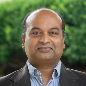 Headshot of WVU expert Anurag Srivastava. He is pictured with green trees in the background and is wearing a dark jacket over a light blue dress shirt. He has receding, dark hair. 
