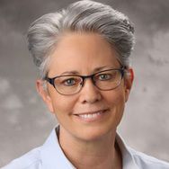headshot of smiling woman with grey hair and glasses