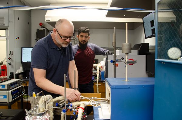 WVU researcher Edward Sabolsky wearing a navy blue golf shirt and classes works with instruments in his lab alongside a fellow researcher. 