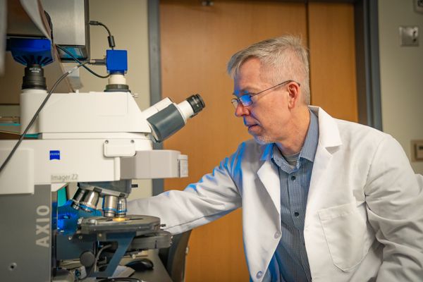 photo of man in white coat looking through microscope