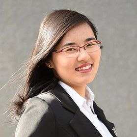 Headshot of WVU researcher Yuhe Tian. She is pictured standing in front of a concrete wall wearing a black jacket over a white dress shirt. She has medium length brown hair and wears glasses. 