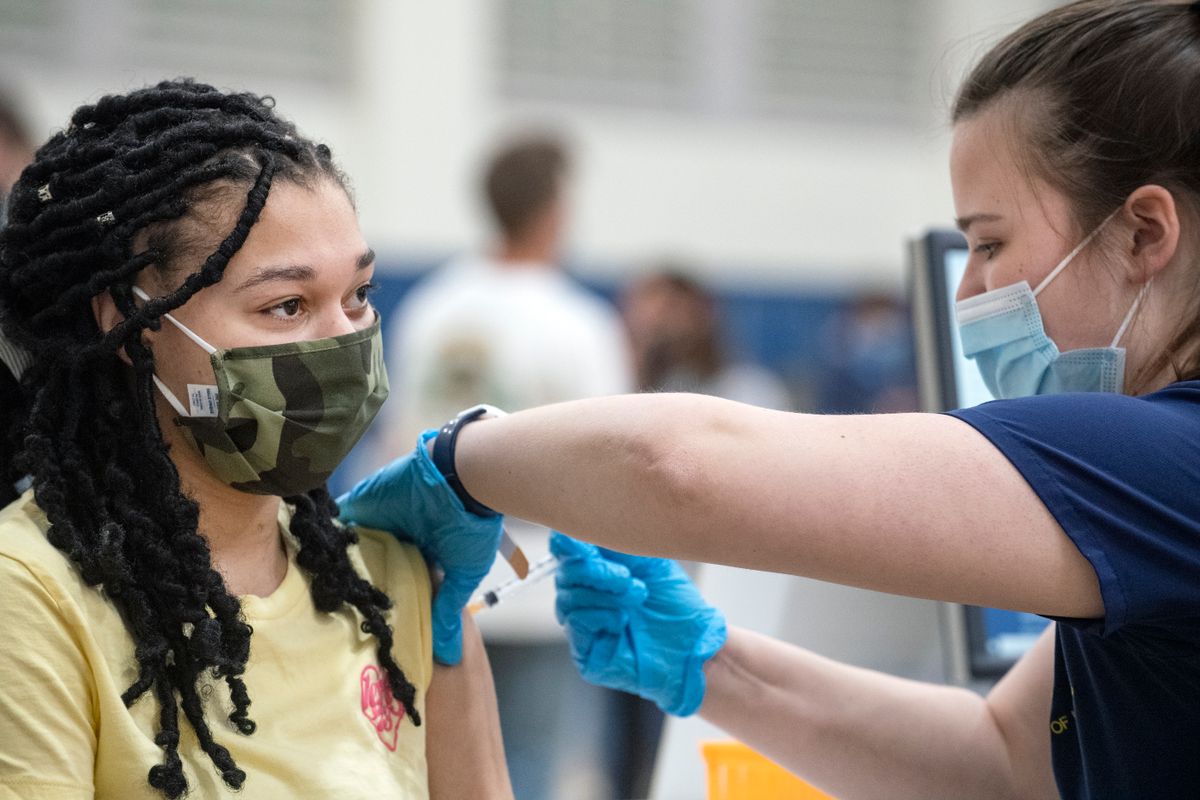 Woman wearing a mask gives a vaccine to another woman wearing a mask.