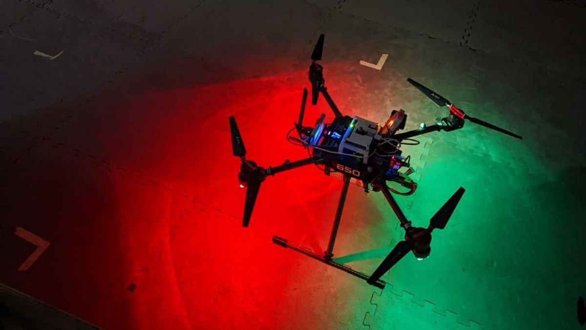 A black drone sits on the ground and is lit with the colors of red and green.
