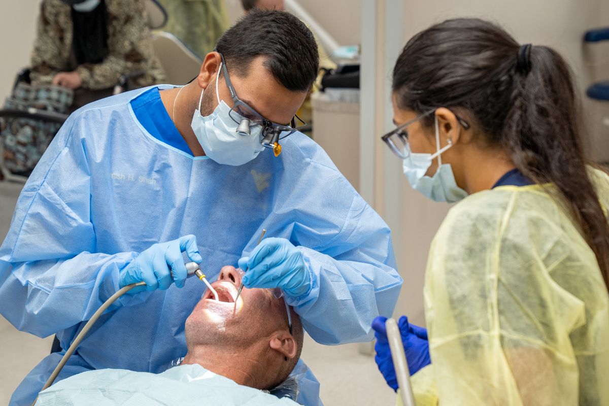 A photograph showing two people connected to the WVU School of Dentistry working on a patient. 