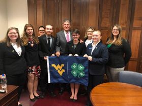 group of smiling people in suits with WVU flag in front of them