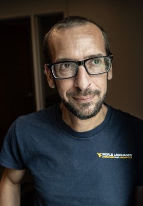 Headshot of WVU researcher Jonah Katz. He is standing against a wall wearing a WVU-branded T-shirt. He has very short hair and wears square-framed glasses. He also has dark facial hair. 