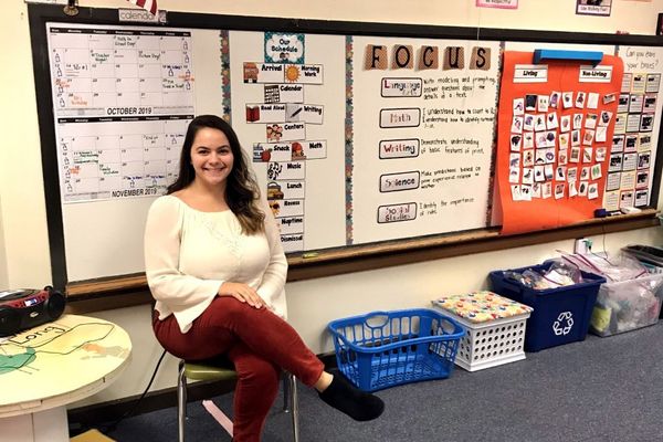 young woman sits by a white board filled with calendars and other educational material