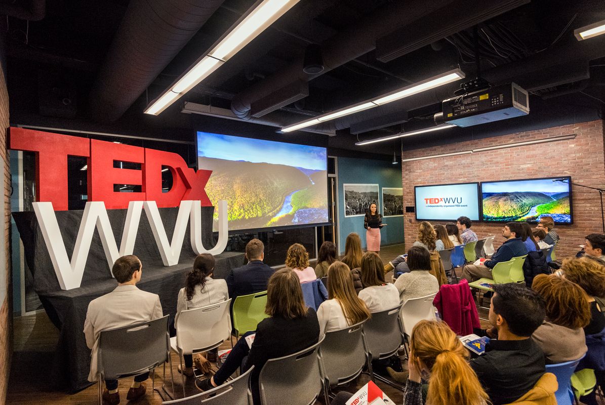 a woman talks to a group of people TEDX (in red) WVU (in white)
