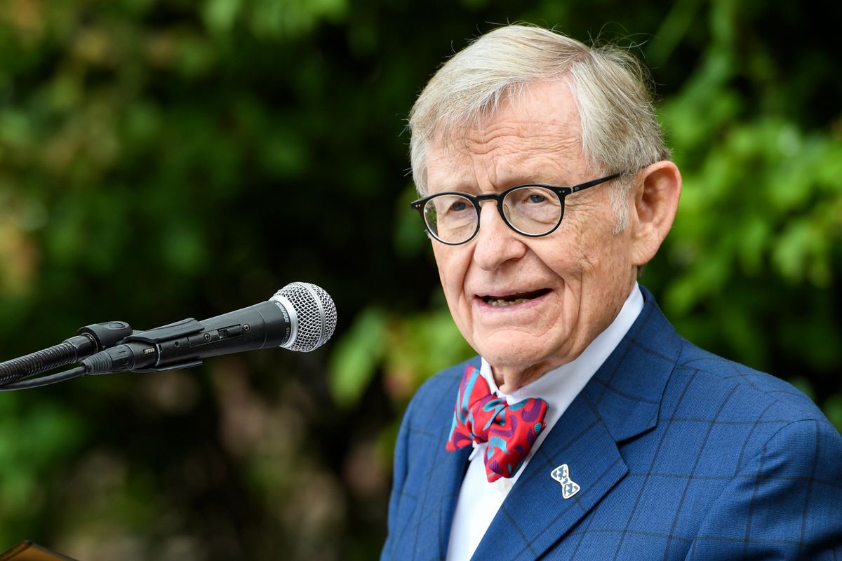 Man wearing glasses and a bow tie stands at an outdoor podium. 
