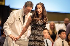 A man in a white coat helps a young woman don her white coat