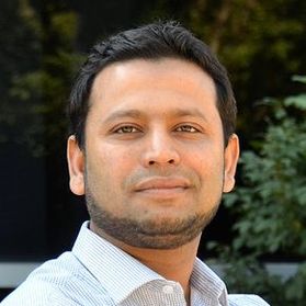 Headshot of WVU professor Omar Abdul-Aziz. He is pictured outside with greenery in the background. He is wearing a white dress shirt and has dark, short hair. He has a very light beard. 