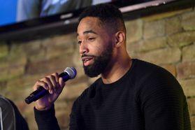 Black man with beard speaks into microphone