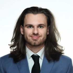 Headshot of WVU researcher Hunter Barber. He is pictured against a white background wearing a blue suit jacket, white dress shirt and black tie. He has long brown hair and a light beard. 