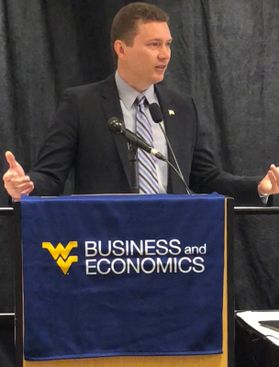 man standing in black suit and grey tie with WV Business and Economics banner 