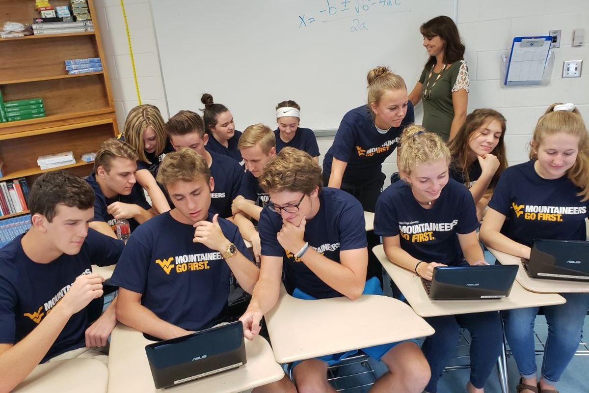 Group of high school students sitting and desks and looking at laptops.