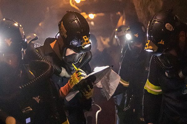 Three WVU students are show in a dark mining setting wearing hard hats and recording data.
