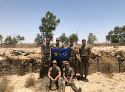WVU student veteran Ben DeRoos is pictured here with five other fellow soldiers in the desert during a deployment. They're holding a WVU flag. 