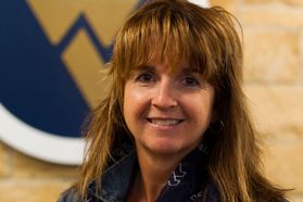 Headshot of WVU professor Christine Schimmel. She is pictured inside with a Flying WV plaque on the wall behind her. She has long, light brown hair with bangs. 