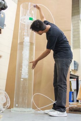 Man standing next to a glass tube filled with water.