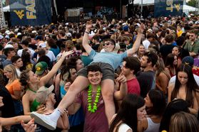 WVU students enjoy a concert on campus. Hundreds of students are shown in the photo including a male sitting on the shoulders of another male. 