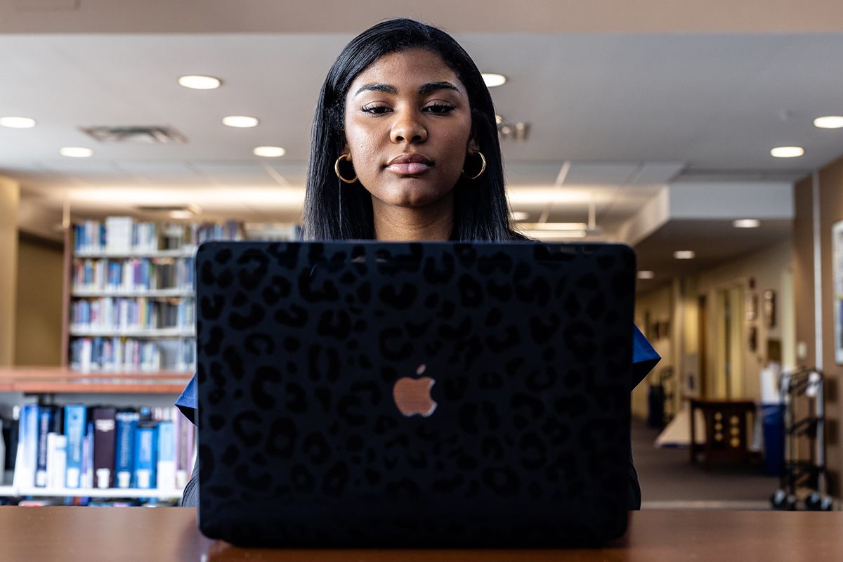 A girl sits in a library staring down at a black macbook