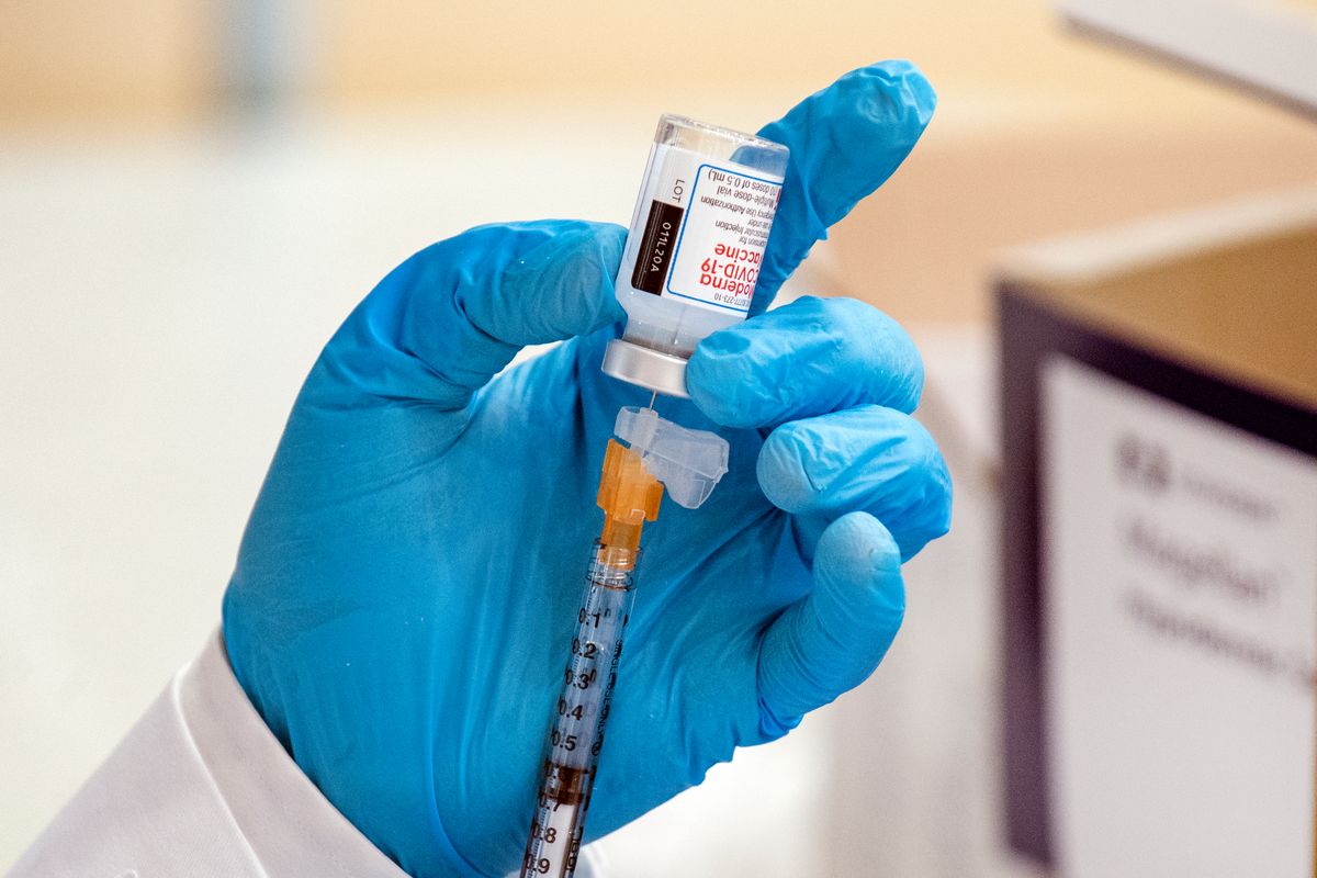 A person in blue gloves prepares a dose of the COVID vaccine