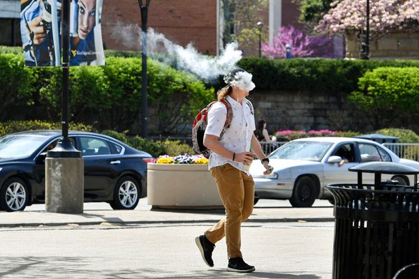 person vaping outside on street, cars in background