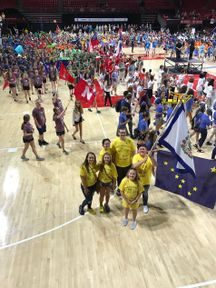 Six students standing in yellow shirts with flag in a gymnasium