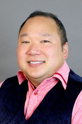 Headshot of WVU professor Sean Tu. He has short dark hair and is wearing a dark colored sweater vest over a pink button up shirt. He is smiling in the photo. 