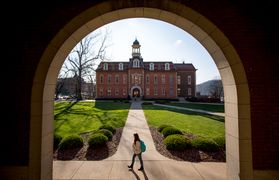A student walks past an arched window that looks out onto Woodburn Circle. Martin Hall is in the background.