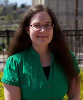 Headshot of WVU researcher Katie Corcoran. She is pictured outside and is wearing a green shirt and glasses. She has long dark hair. 