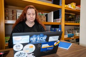 A female worker uses a laptop full of stickers to work on behalf of The Rack, the food pantry on the WVU Campus. 