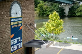 The entrance to the equipment rental area of the Morgantown Adventure Outfitters Rental Center. The mon River can be seen in the background with at least two people in the water on paddleboards. 