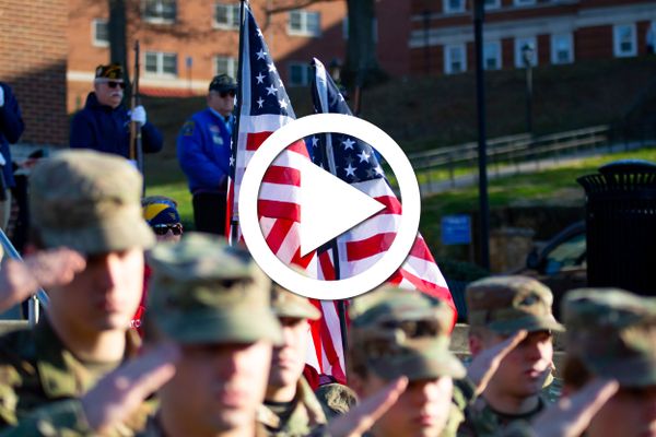 soldiers salute in front of flags with play button super-imposed