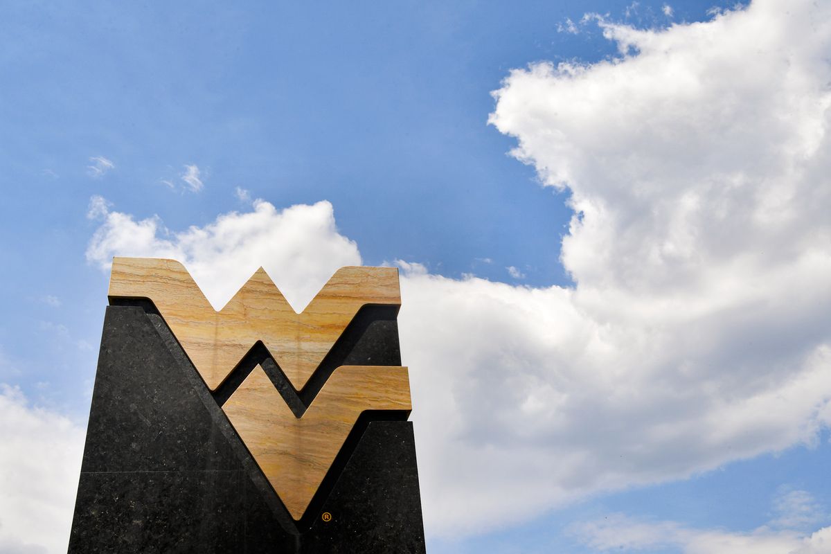A marble monument made from the WVU logo, the Flying WVU with blue sky and white wispy clouds overhead. 