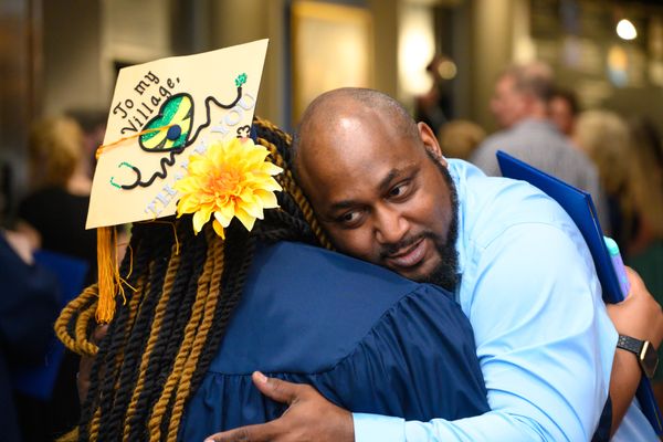 A WVU grad hugs her father wearing a decorated mortar board that says: To my village, thank you. 