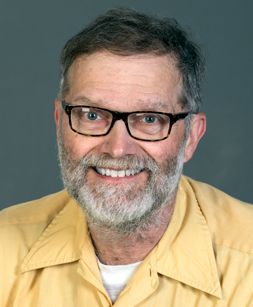 Headshot of WVU researcher James Kotcon. He is pictured wearing a yellow, button-up shirt, dark-framed glassed, dark hair and a gray beard.