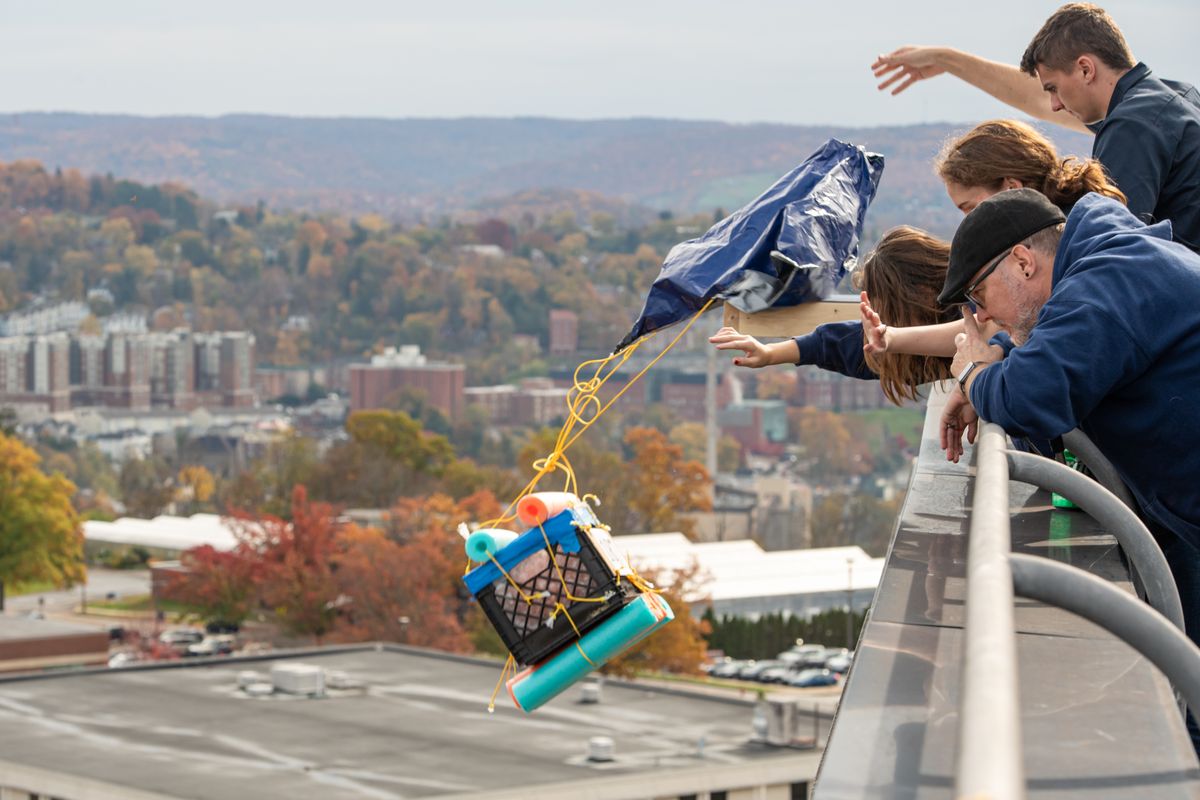 Competitors watch as a milk crate container protecting a pumpkin is dropped off the roof of the WVU Engineering Sciences Building.