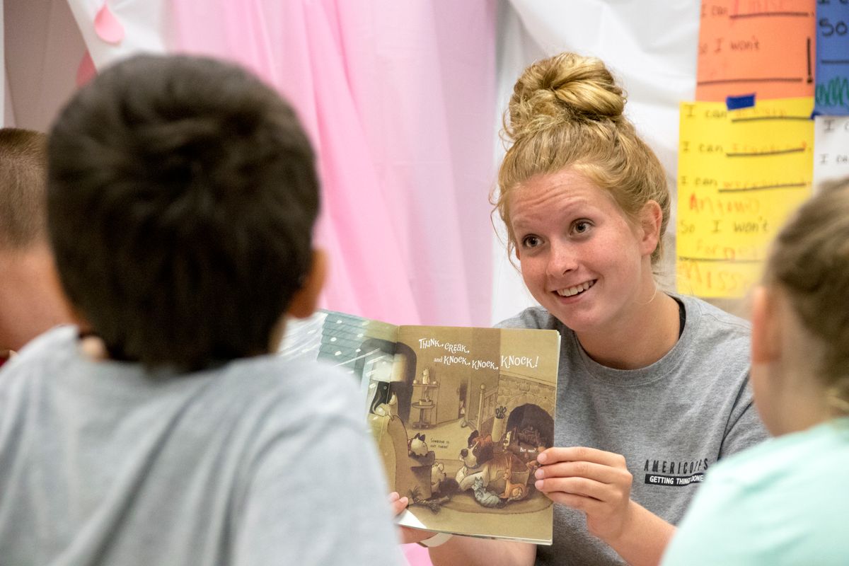 A blonde woman with her hair in a bun reads to students