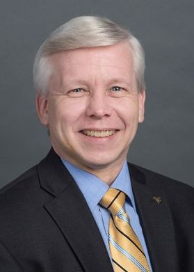 This is a portrait of Scott Tobias who is wearing a black jacket, blue shirt and gold tie.