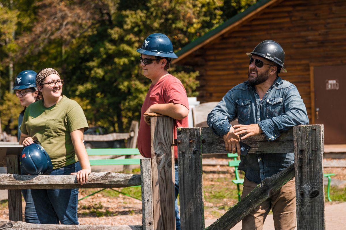 woman and two men stand in hard hats along a wood fence