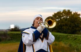 a young girl in a white hat and WV marching band uniform walks towards the camera playing a trombone