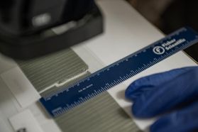 An image showing the forensic examination of two duct tape edges. The two tape pieces are on a white surface and a blue ruler is being used. A blue gloved hand can also be seen in the frame. 