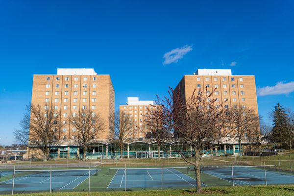 three large brick buildings set against a bright blue sky and blue tennis courts in the foreground